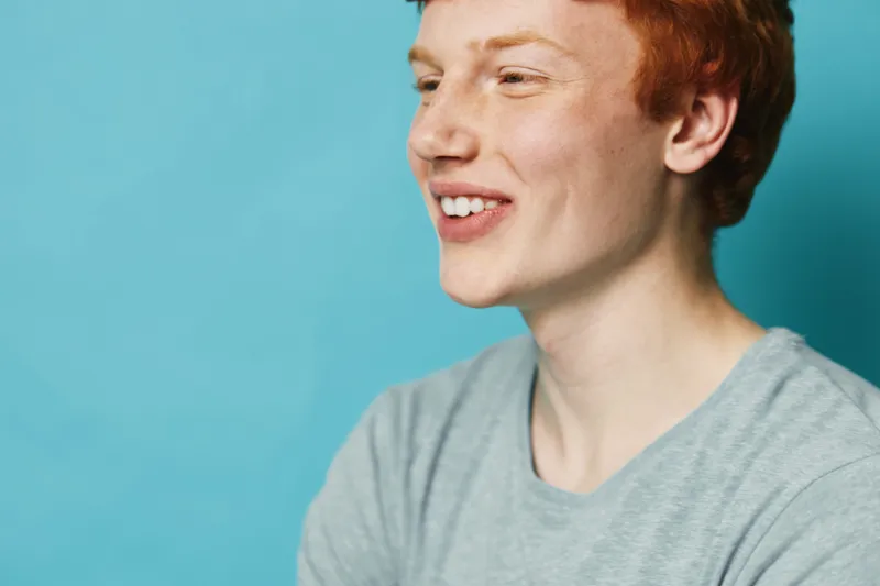 Young man with red hair smiling and looking away on blue background. Casual clothing and happy expression for lifestyle, portrait and positive mood.