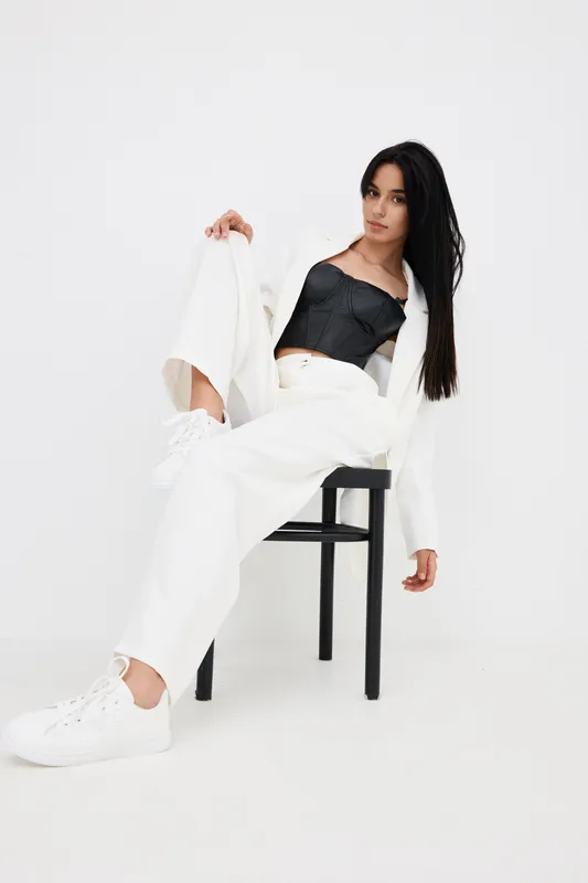 stylish woman posing confidently in white outfit with black top and sneakers, long dark hair and minimalistic studio background, modern fashion look