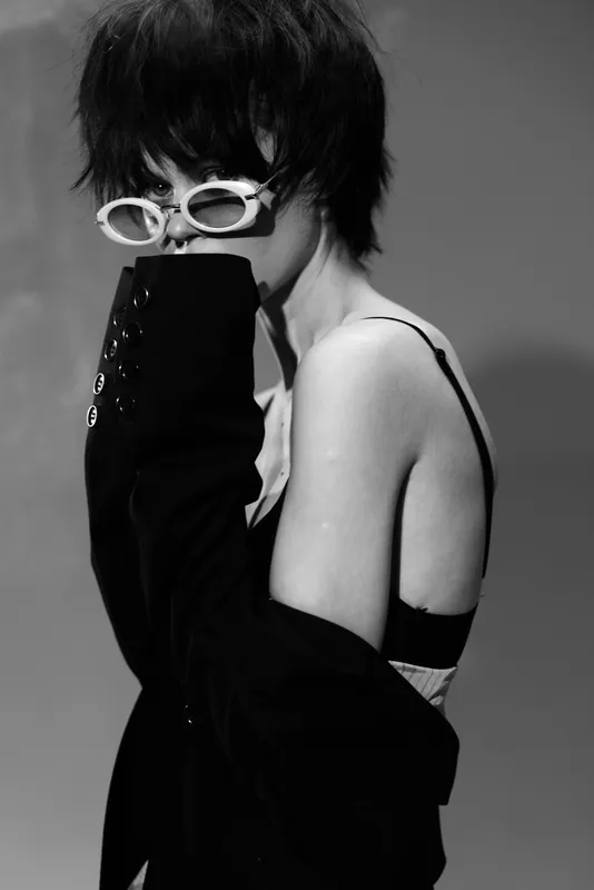 Stylish woman with short hair wearing sunglasses in black and white portrait with moody expression and soft lighting.
