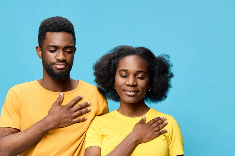 A joyful African American couple in matching yellow shirts posing against a bright blue background, expressing gratitude and unity through their emotions