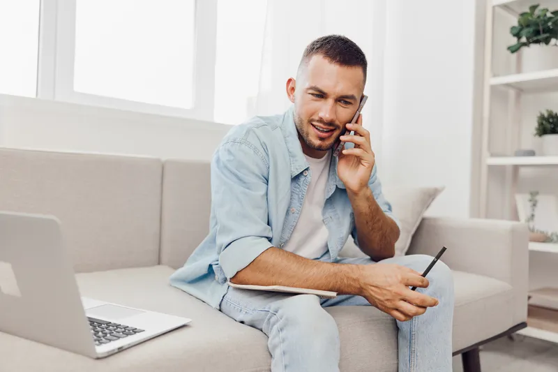 Smiling man engaged in a phone conversation, showcasing modern home office vibes with workspace and cozy background, reflecting productivity and connection.