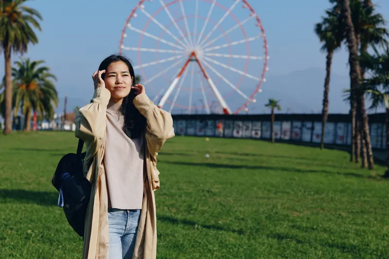 woman outdoor park ferris wheel coat travel casual happy scenery smile sunlight greenery palm trees amusement background fashion casualwear breeze day leisure lifestyle landscape waterfront skyline