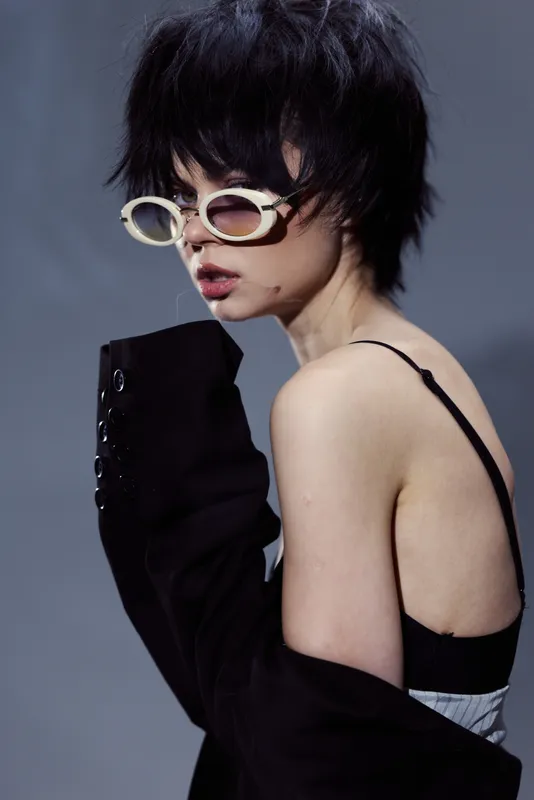 Stylish woman with short black hair wearing white sunglasses and a trendy black jacket, showing confident and edgy fashion look.