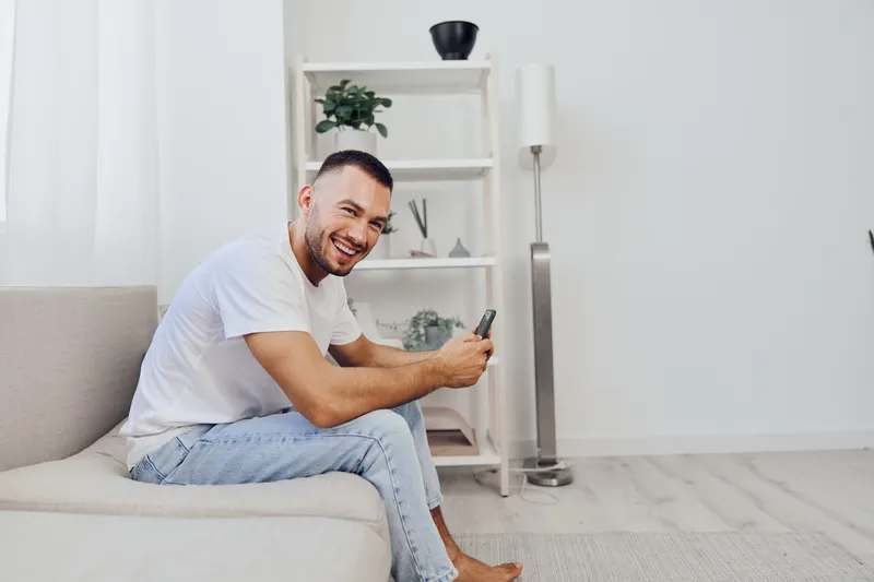 Smiling man enjoying a microbreak while on his phone, showcasing the balance between work and personal life in a modern home environment.
