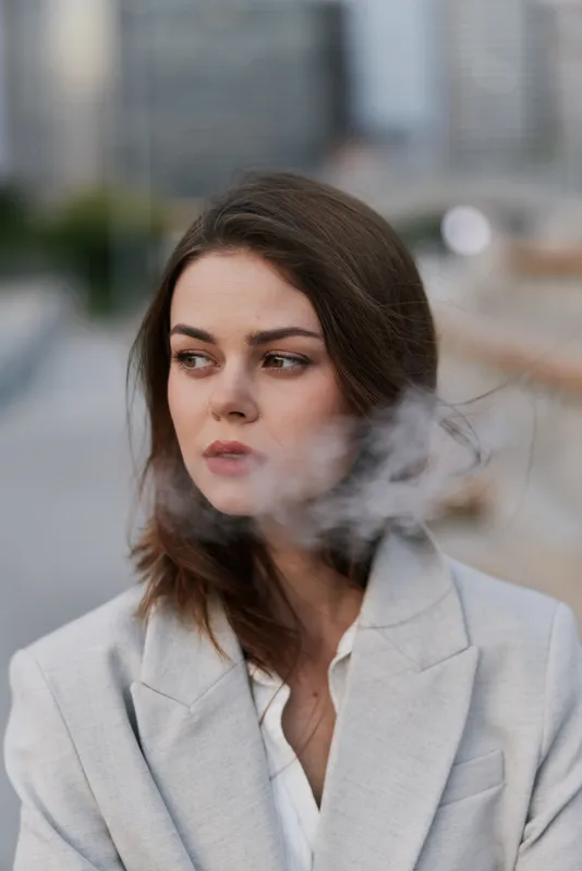 Young woman in light gray blazer with pensive expression and smoky atmosphere, urban city background, emotional business concept
