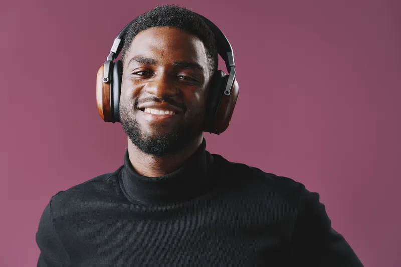 Happy young Black man wearing stylish headphones, enjoying music against a purple background, showcasing modern lifestyle and relaxation