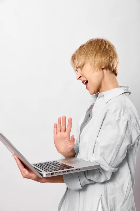 Child laptop stop gesture shouting panic indoors white shirt studio portrait, boy holds computer with one hand raised, surprised worried expression, minimal background