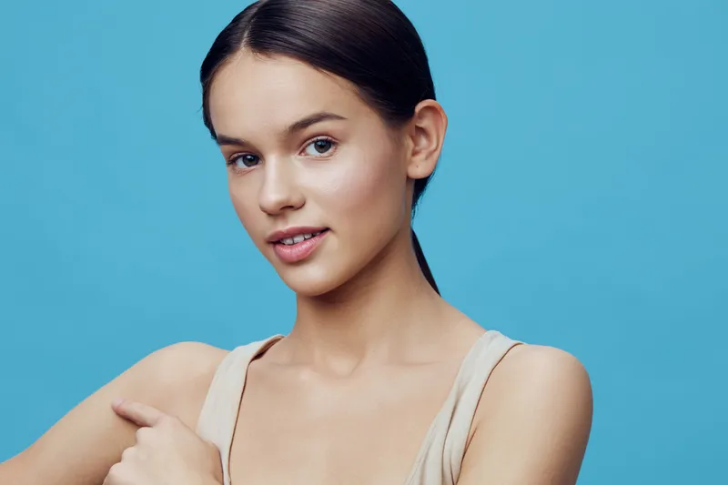 Portrait of a young model with a natural look against a vibrant blue background, showcasing healthy skin and a serene expression