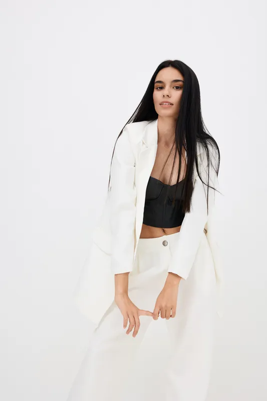 Woman posing in white suit and black top with long dark hair, stylish outfit, modern fashion, minimalistic studio background, youthful and confident vibe.