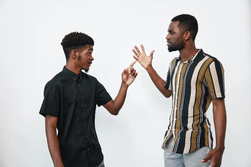 Two african american men with dark skin having a serious conversation in casual clothes on white background. Young black males discussing and gesturing indoors.