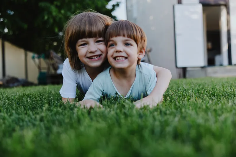 Two smiling children enjoying time together outdoors in the green grass, filled with happiness and joy during a sunny day in the park.