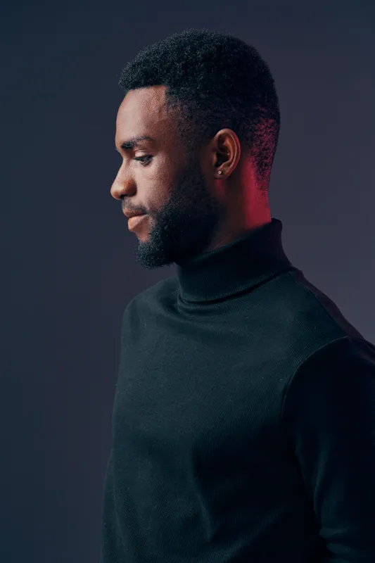Portrait of a contemplative young Black man in a black turtleneck, showcasing a side profile expression against a gradient background
