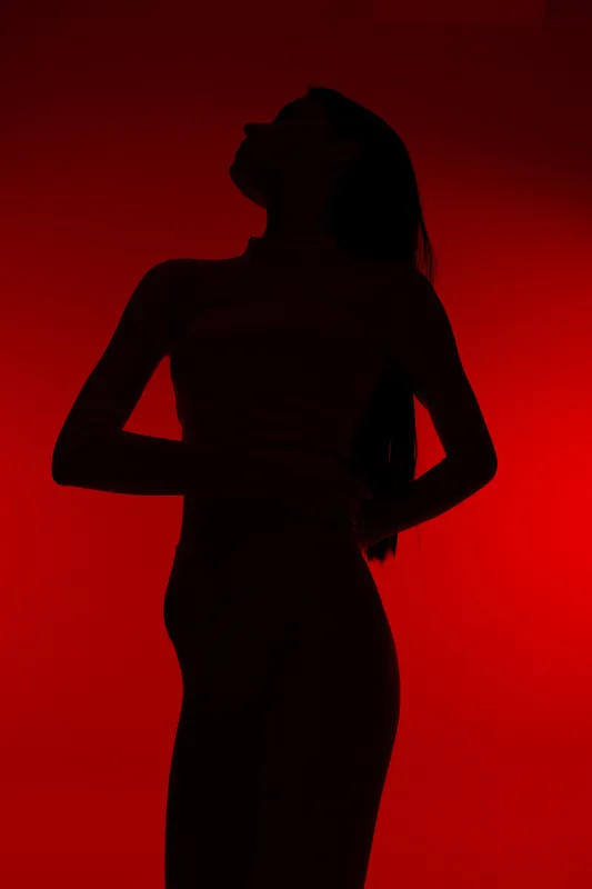 Silhouette of a woman sport fitness posing against a vibrant red background, highlighting her toned figure and athletic posture for a powerful, dynamic look.