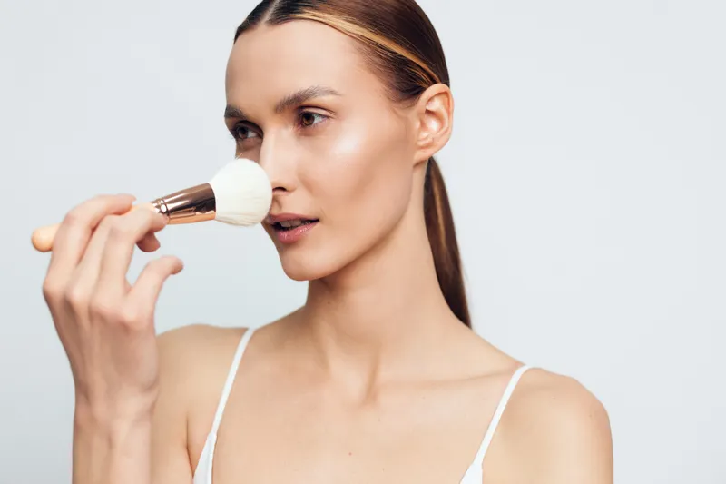 Young woman with clear skin applies powder on her face using makeup brush isolated on white background natural beauty concept skincare routine female portrait
