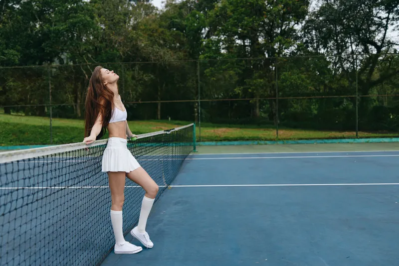 Young female tennis player in sporty outfit enjoying the moment on a sunny court, showcasing athleticism, energy, and confidence with a backdrop of lush greenery