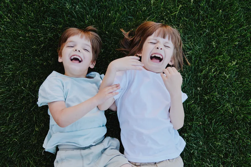 Happy children laughing on green grass, enjoying a sunny day, playing together, showing joy and friendship in a natural setting.