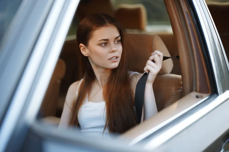 Young woman in a car, looking concerned while fastening her seatbelt, with soft natural light creating a calm atmosphere. Comfort, safety, and attention are highlighted.
