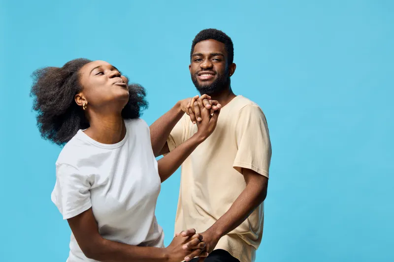 Joyful couple dancing together against a blue background, showcasing love and happiness in casual clothing The vibrant colors enhance the playful mood
