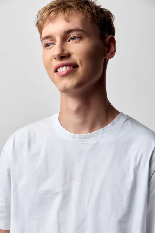Young man, smile, casual, white t shirt, bright background, relaxed pose, everyday fashion, simple clothing, clean lighting, neutral backdrop, head and shoulders, studio look, natural light, cheerful