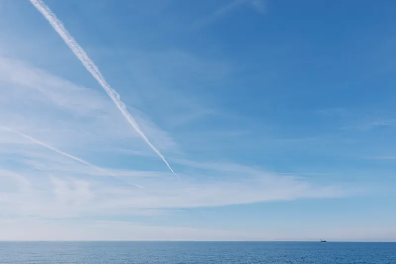 Calm ocean landscape with a wide horizon, clear blue water and a single contrail across the sky, evoking tranquility and vast possibilities for exploration