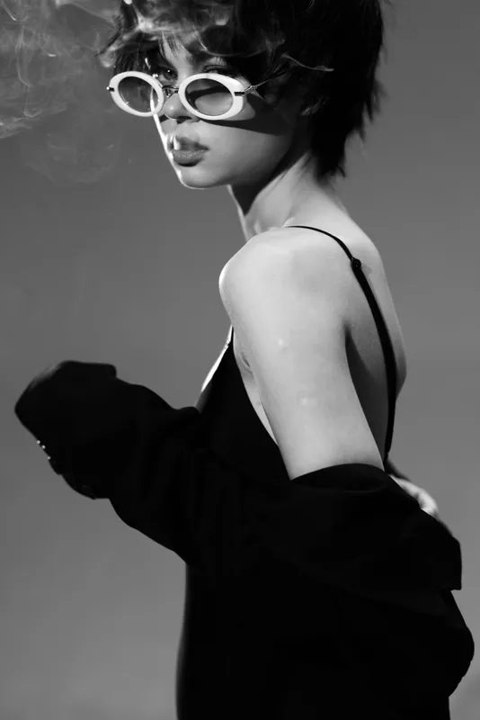 Stylish black and white portrait of a woman wearing sunglasses and a dark off-shoulder garment with a moody expression.