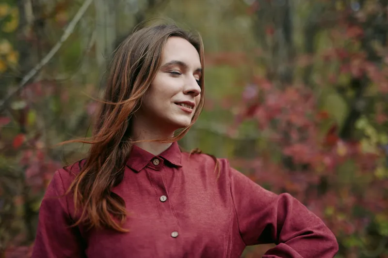 Close portrait of a young woman in an autumn wood, natural expression and relaxed posture capturing a genuine presence and truthful emotion in a simple authentic lifestyle scene.