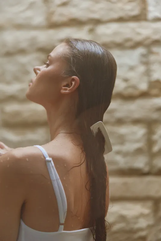 woman combing wet hair in shower with stone wall background, natural skincare, relaxing moment, calm and serene atmosphere, self-care routine