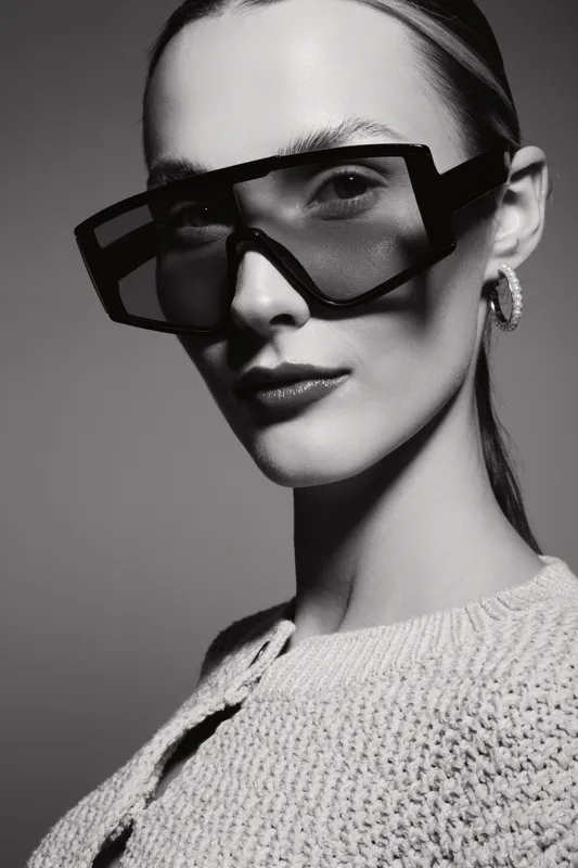 Portrait of a light skinned white woman wearing oversized glasses and knitwear. Studio shot in black and white with soft lighting and sharp focus.