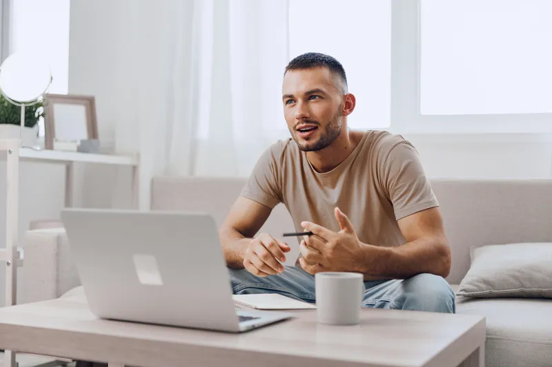 Engaged man sitting at a desk, working on a laptop and discussing ideas. The modern setting and expressive demeanor highlight creativity and collaboration in a cozy space.