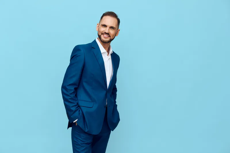 A confident business professional stands against a solid blue background, exuding optimism and focus. The isolated color backdrop highlights a polished man in a tailored suit, ready for leadership