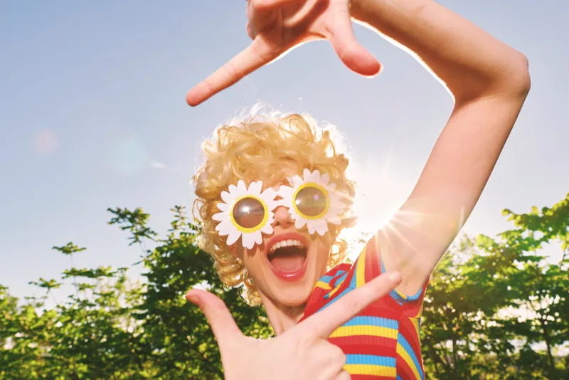 Cheerful child outdoors, laughter, colorful retro film sunshine moments, daisy sunglasses, striped shirt, nature background, lively mood, candid charm, bright and playful