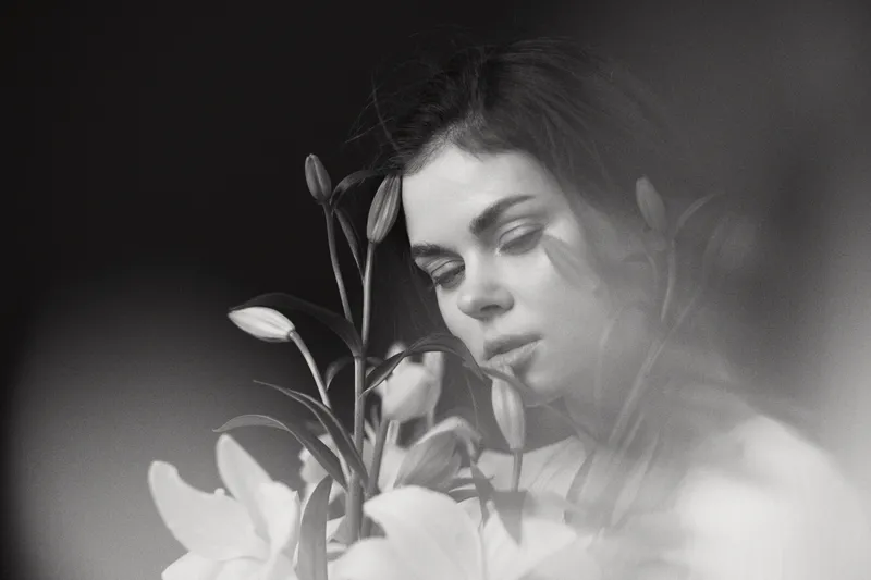 A contemplative young woman surrounded by white lilies, showcasing serenity and elegance in a black and white portrait