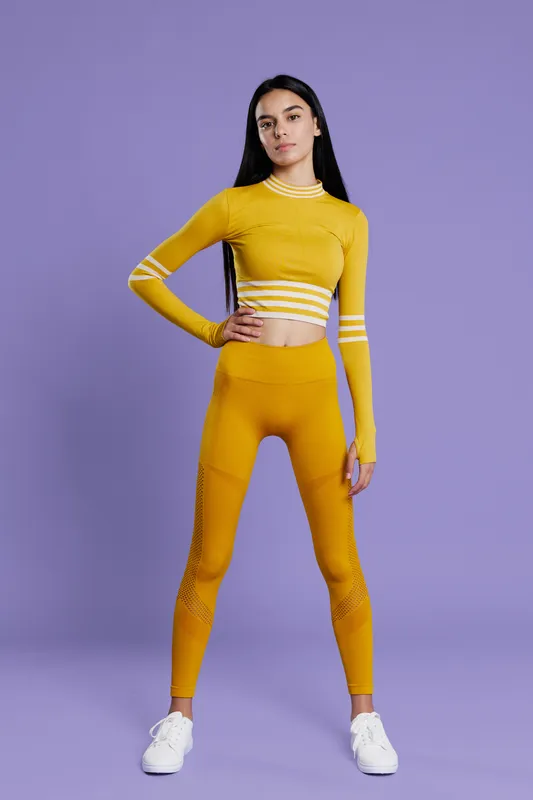 Sport fitness woman standing full-length in yellow activewear against a purple background, showcasing a confident pose and athletic style for healthy lifestyle concepts.