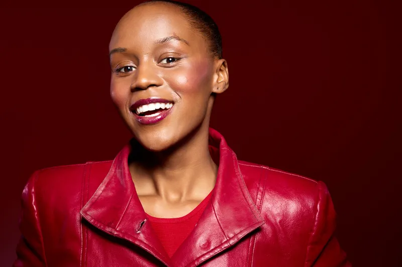 Confident dark skinned African woman wearing a red leather jacket smiles brightly on a red background. Concept of beauty, fashion, joy, and empowerment for black women.