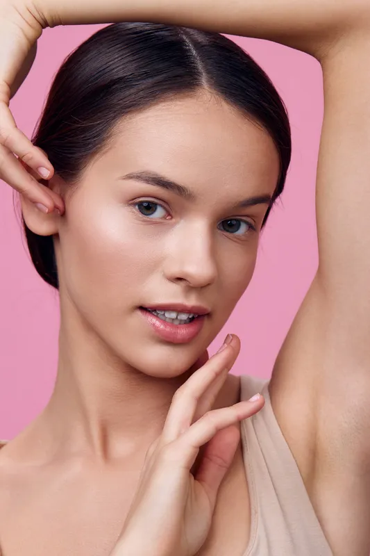 Young woman with flawless skin posing elegantly against a pink background, showcasing natural beauty, soft makeup, and a serene expression, perfect for beauty and skincare concepts