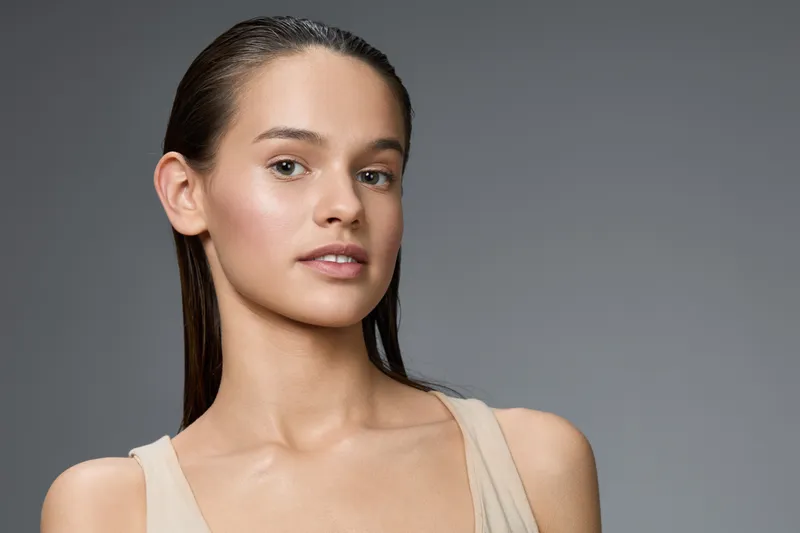 Young woman with smooth skin and natural makeup, showcasing beauty and confidence against a minimalistic gray background