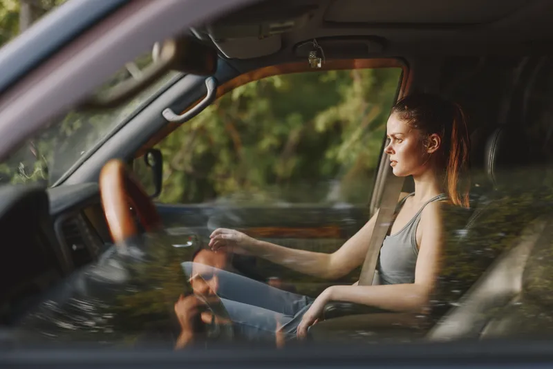 Young woman in casual outfit sitting in a car, contemplating outdoors with serene expression, light colors, nature background creating a peaceful vibe
