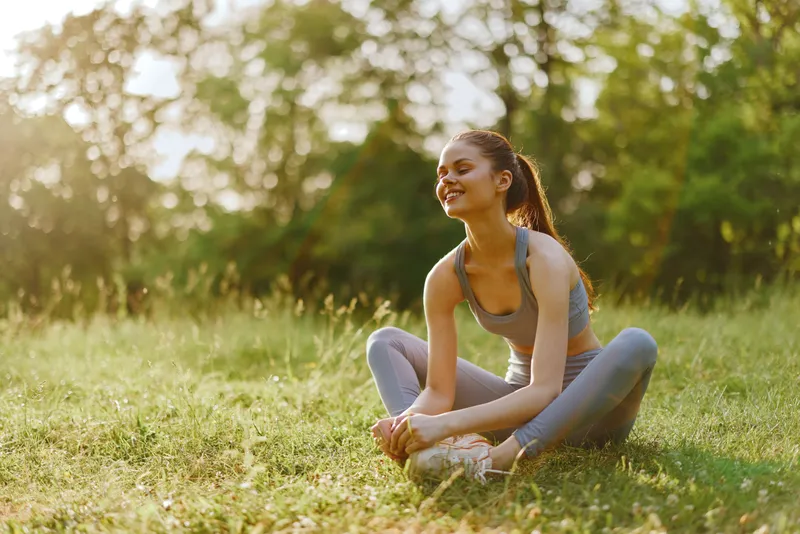 Young woman enjoying a moment of relaxation in nature, wearing athletic clothing, representing health, fitness, and joyfulness in a sunny outdoor setting