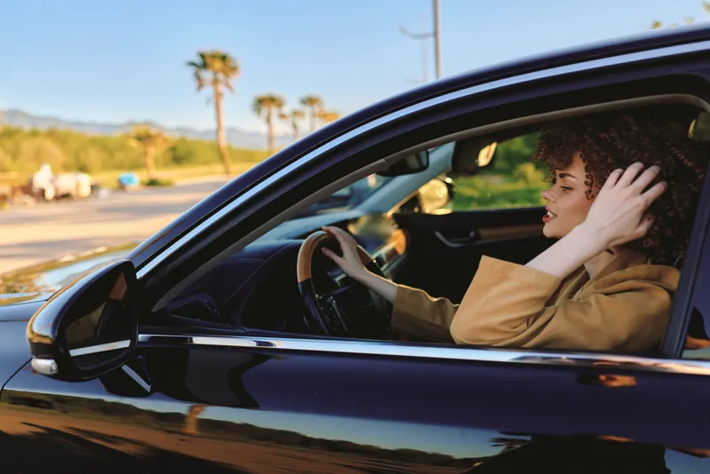 A stylish woman sits in a sleek car, relaxed and reflective, enjoying a casual drive. Warm retro film colors create a nostalgic, everyday lifestyle moment.