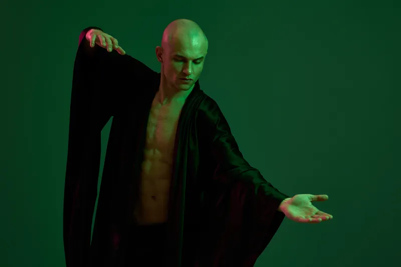 Black and white image of a man performing graceful dance moves, showcasing strength and emotion with dramatic lighting and a captivating pose.