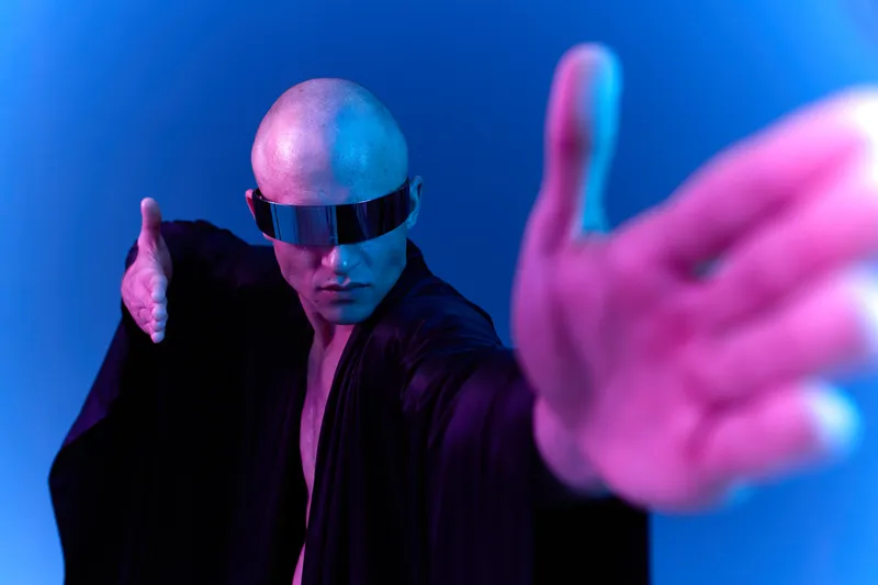 A futuristic man in a black robe reaches out with a striking pose. His sunglasses and bald head enhance the otherworldly feel in this vibrant color light image.