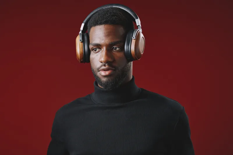 Focused young man wearing stylish headphones, showcasing a modern vibe and deep concentration against a red background
