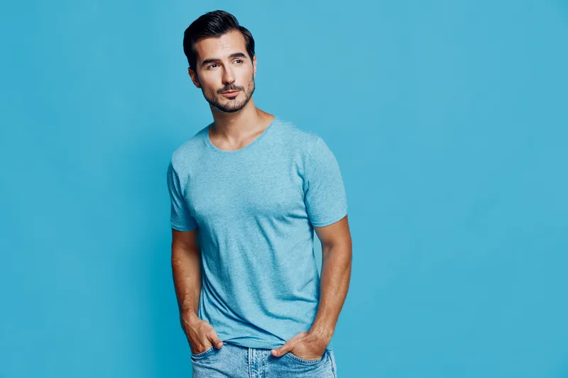 Confident young man wearing a light blue t-shirt poses against a vibrant blue background, showcasing a casual and relaxed style. Modern lifestyle concept.