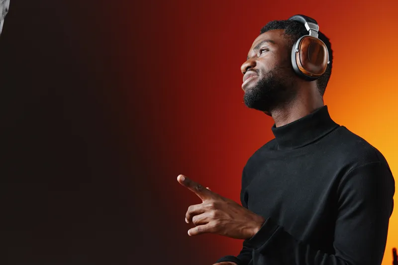 Young Black man enjoying music with headphones, smiling expressively against a warm gradient background, showcasing joy and relaxation in a modern setting