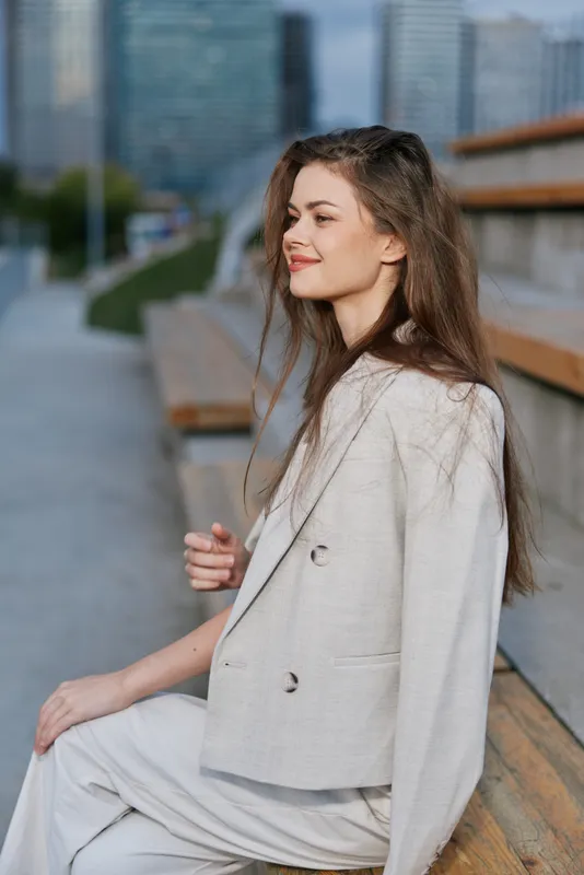 Businesswoman in a modern city setting, dressed in a stylish light-colored blazer and pants, exuding confidence and professionalism.