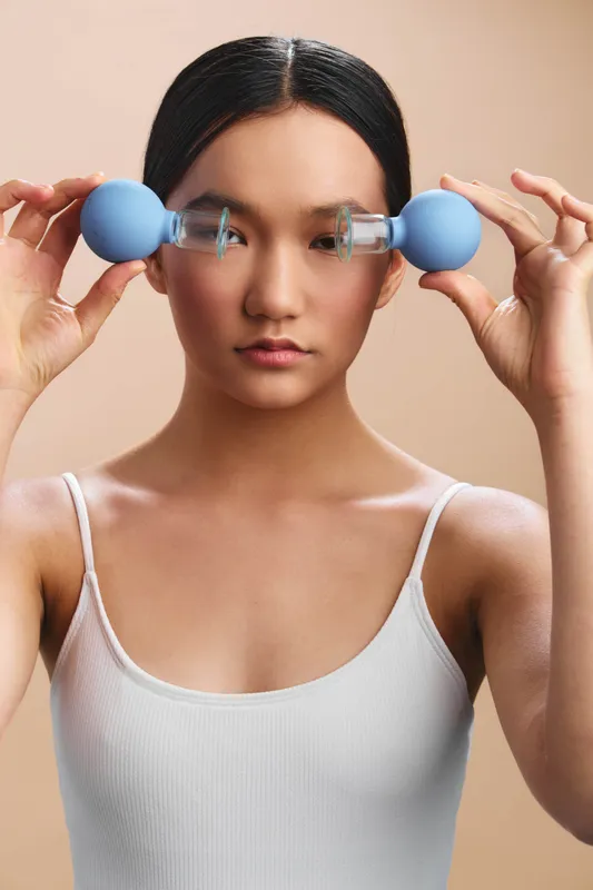 asian woman lifts small dumbbells close to her face in a studio setting, focusing intently with a calm expression to convey balance, control, and fitness mindset.