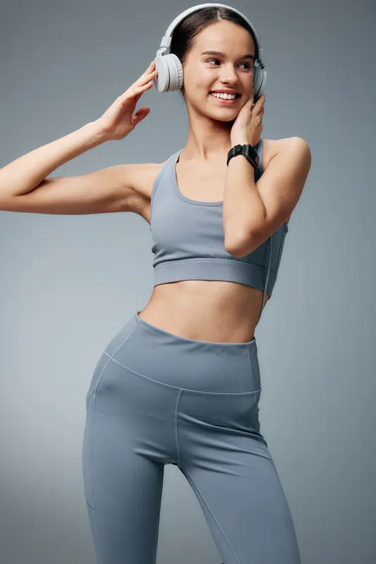 Fitness woman in athletic wear with headphones, smiling as she poses mid workout in a studio. A dynamic scene capturing energy, focus, music, and an active lifestyle.