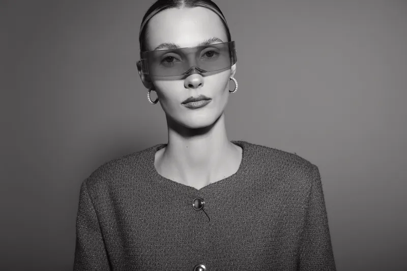 Portrait of a young Caucasian woman with pale skin wearing oversized sunglasses and wool coat, posing in studio with dramatic lighting. Concept of fashion and elegance.