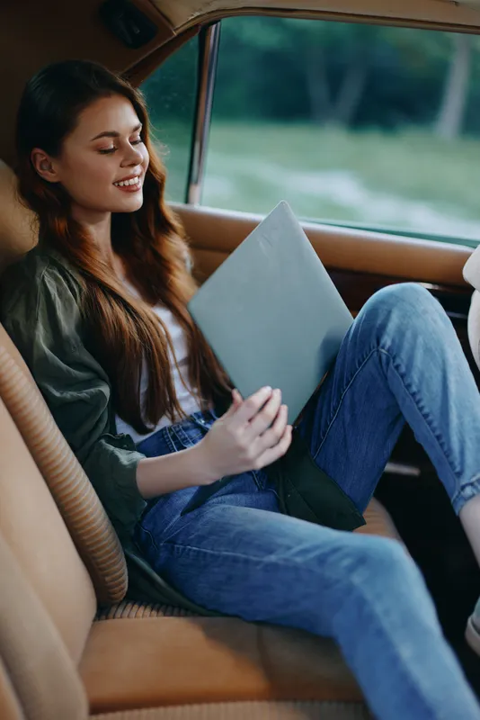 Young woman relaxing in a vintage car, wearing casual outfit, showcasing emotions of happiness and calmness, colorful natural background, ideal for lifestyle themes.