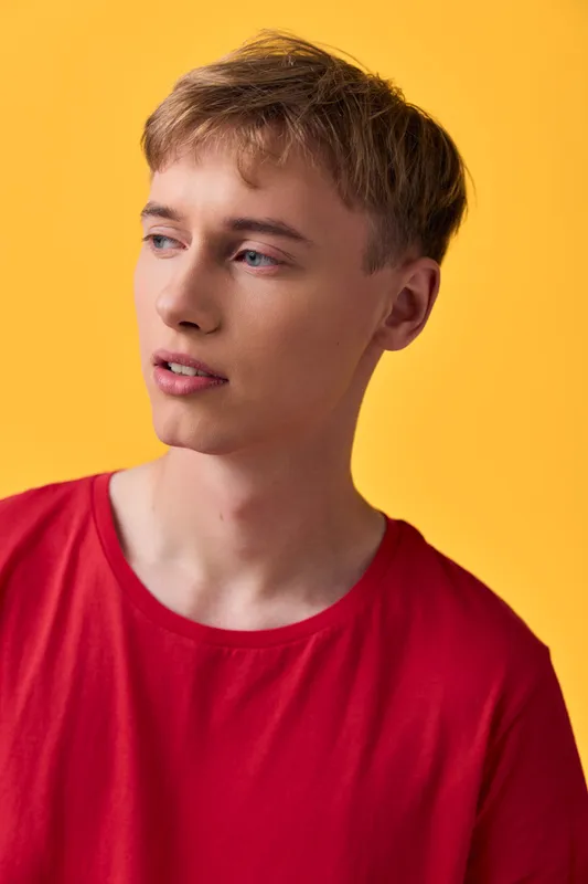 Young man in a red shirt posed against a yellow background in a studio setup, with soft shadows and natural skin tone, conveying a calm modern mood for lifestyle shoots